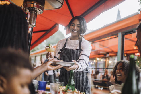 Smiling waitress serving food and drinks to customers having fun at restaurant - MASF41812