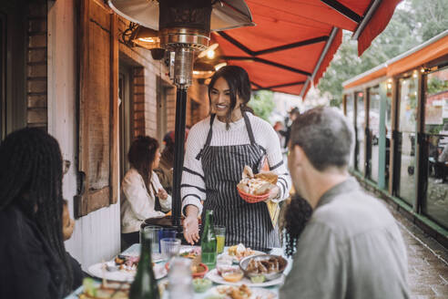 Smiling waitress talking to family having food at restaurant - MASF41814