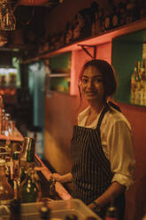 Portrait of smiling female bartender wearing apron and standing at bar - MASF41822