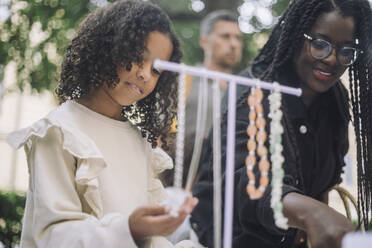 Low angle view of girl buying jewelry with mother while shopping at flea market - MASF41824