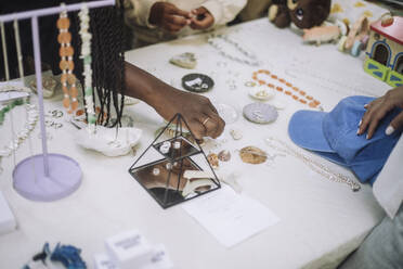 Woman buying accessories arranged on table while shopping at flea market - MASF41825