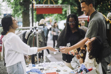 Side view of happy female vendor laughing while taking online payment from customer at flea market - MASF41826