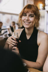 Portrait of smiling woman holding drink bottle at restaurant - MASF41843