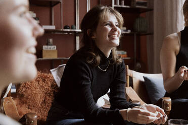 Smiling young woman looking away while sitting with friends in apartment - MASF41853