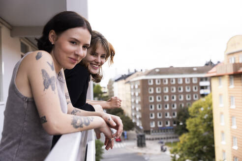 Smiling female friends looking away while leaning on railing in balcony - MASF41861