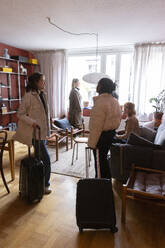 Young female tourists standing with wheeled luggage in living room at apartment - MASF41867