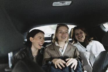 Happy female tourists sitting on back seat in car during road trip - MASF41892