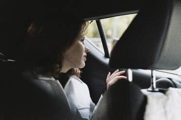 Young female tourist looking through window while sitting in car on vacation - MASF41895