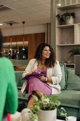 Smiling female business professional sitting with file on sofa at office - MASF41914