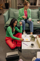 High angle view of smiling business professional writing in book while sitting near female colleague at office - MASF41928