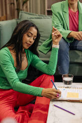 Businesswoman writing in book while sitting near female colleague at office - MASF41929