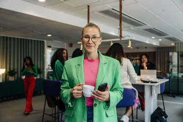 Portrait of smiling mature businesswoman holding coffee cup at office - MASF41933