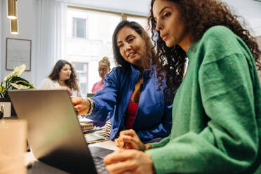 Businesswoman explaining female colleague over laptop at office - MASF41945