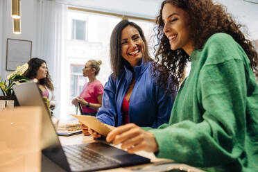 Happy businesswoman with smiling female colleague looking at laptop in office - MASF41946