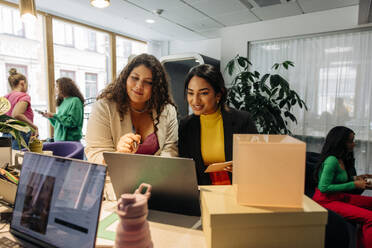 Smiling female entrepreneurs discussing over laptop while working at office - MASF41949