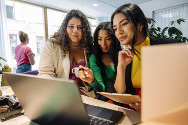 Businesswoman sharing laptop with female entrepreneurs at office - MASF41951