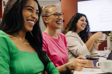 Happy businesswoman sitting with colleagues during meeting at work place - MASF41962