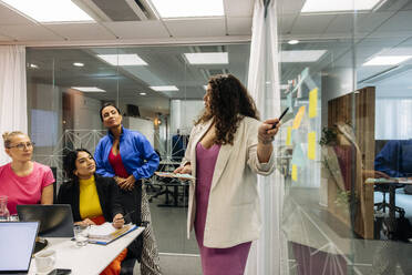 Female entrepreneur explaining colleagues while doing brainstorming session at office - MASF41974