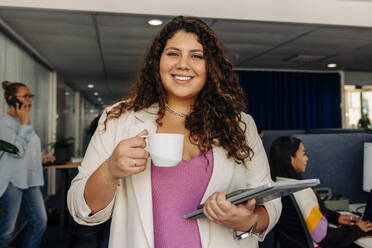 Portrait of smiling female entrepreneur holding coffee cup at office - MASF41997