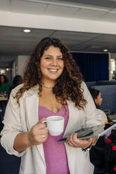 Portrait of smiling young businesswoman holding coffee cup at office - MASF41998