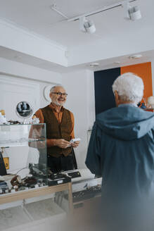 Smiling male antique shop owner talking with customer in store - MASF42020