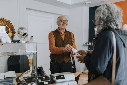 Male antique shop owner giving bill to female customer at counter in store - MASF42024