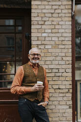 Portrait of happy male owner with coffee cup standing outside store - MASF42029