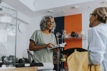 Senior female entrepreneur with credit card reader talking to customer at checkout counter - MASF42030