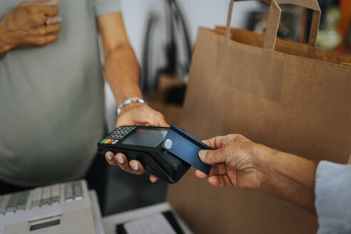 Cropped image of female customer paying through credit card to saleswoman at checkout of antique shop - MASF42032