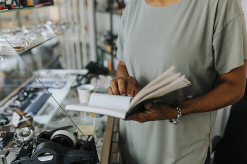 Midsection of saleswoman with diary standing at antique shop - MASF42036