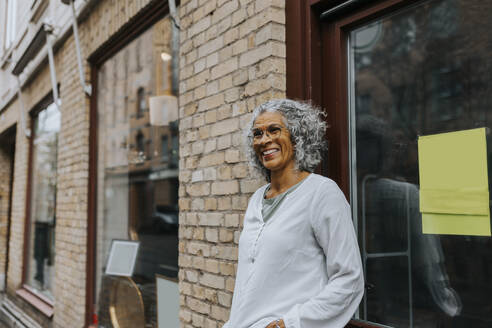 Happy senior female owner standing outside of antique shop - MASF42038