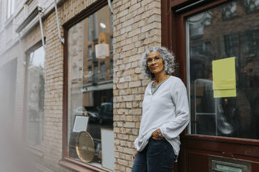 Portrait of senior female entrepreneur with hand in pocket standing outside store - MASF42039