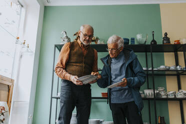 Male customer examining plates held by salesman in antique shop - MASF42040