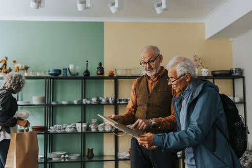 Male owner showing picture frame to senior customer in antique shop - MASF42042