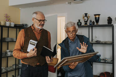 Senior male customer buying picture frame from salesman at antique shop - MASF42043