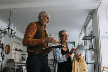 Senior woman examining vase while standing by male owner in antique shop - MASF42044