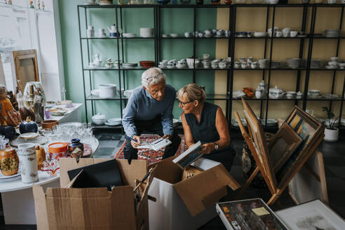 Male and female colleagues discussing while sitting in antique shop - MASF42047