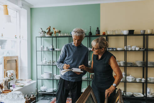 Female and male owners calculating while working in antique shop - MASF42050