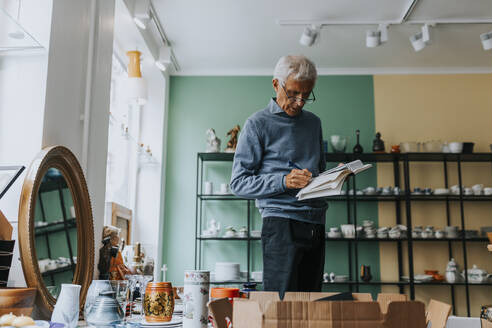 Senior male owner calculating while working in store - MASF42051