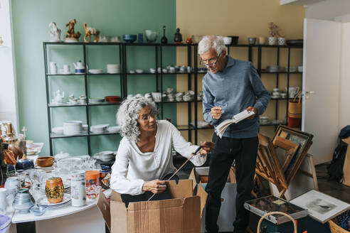 Elderly female entrepreneur analyzing fishing rod with male colleague at antique shop - MASF42052