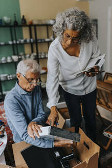 Female owner analyzing box held by male colleague in antique shop - MASF42054