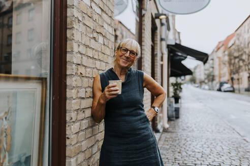 Portrait of smiling saleswoman with coffee cup standing outside store - MASF42061