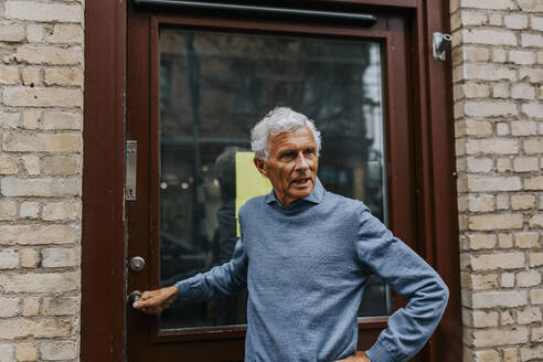 Elderly male entrepreneur standing by door of store - MASF42062