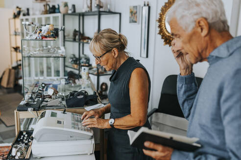 Male and female entrepreneurs standing at checkout while working in antique shop - MASF42064