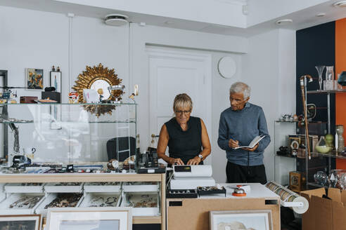 Male and female owners standing at checkout while working in antique shop - MASF42066