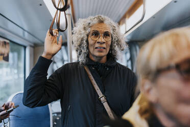 Elderly woman standing in bus while traveling for work - MASF42071