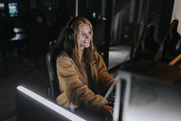 Smiling woman playing video game in illuminated gaming center - MASF42076