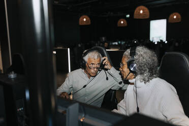 Senior couple talking while wearing headset sitting in gaming lounge - MASF42083