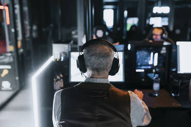 Rear view of senior man playing video game at gaming center during weekend - MASF42111