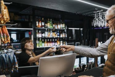 Young saleswoman giving game controller to male customer at gaming lounge - MASF42116